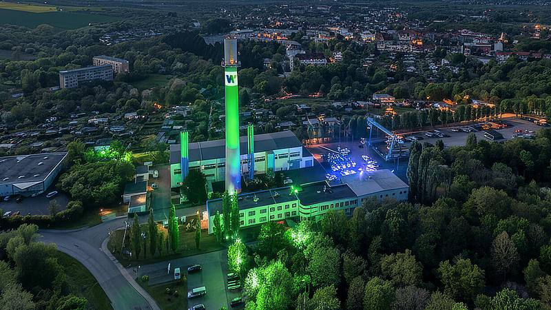 Stadtwerk Weißenfels bei Nacht mit markantem Schornstein ist grün und blau angeleuchtet