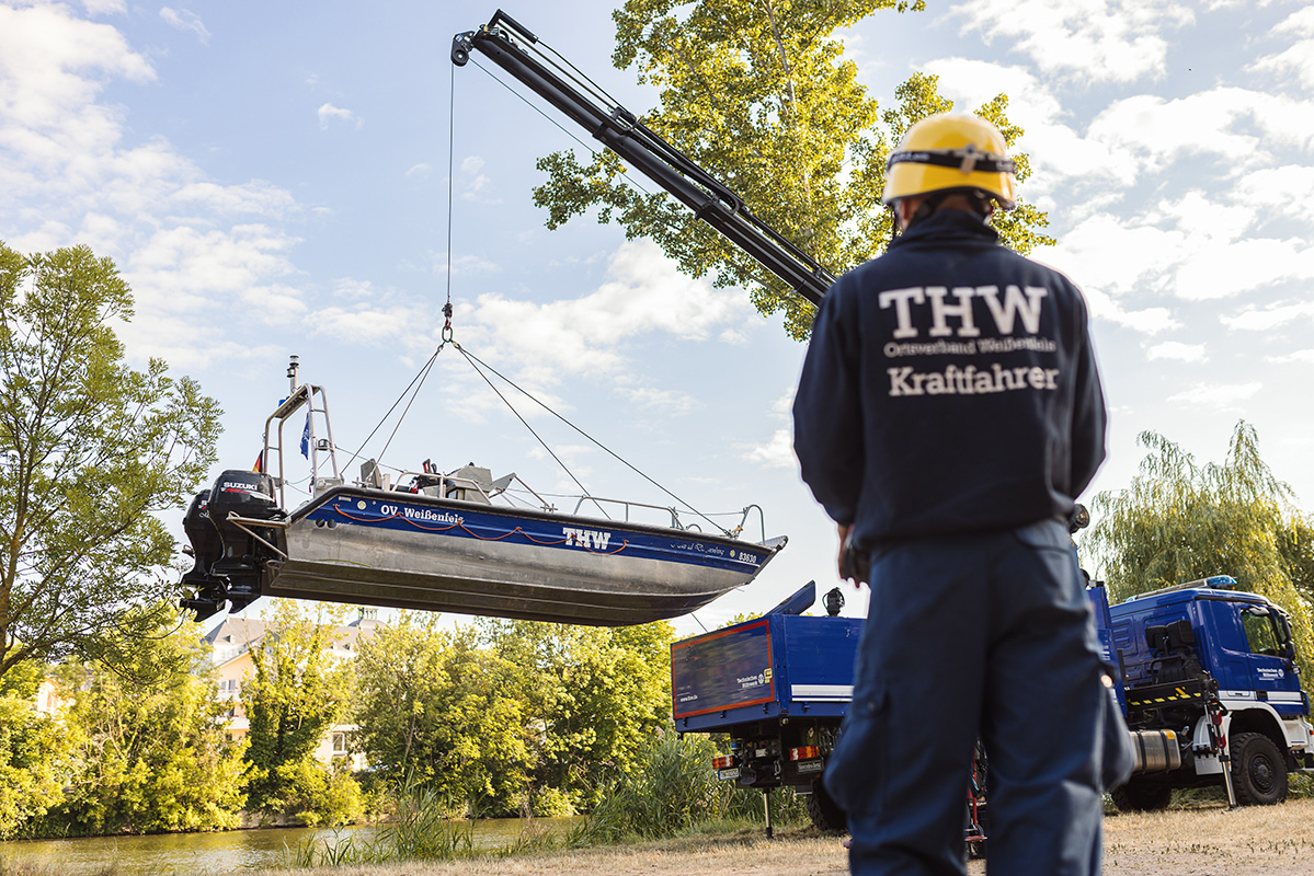 THW Mitarbeiter von hinten zu sehen, wie er ein Boot vom Anhänger eines LKWs mit Fernbedienung ins Wasser hebt