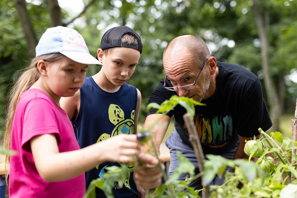 Schulgarteneinsatz, Lehrer mit zwei Schülern schneidet Rosen