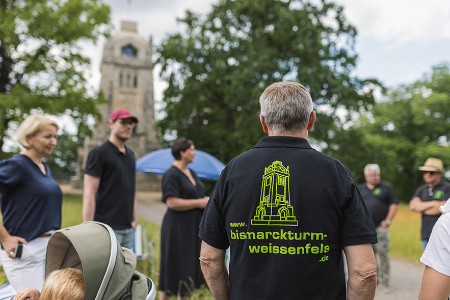 Eineige Festbesucher vor dem Bismarckturm und ein Mann mit T-Shirt und dem Aufdruck des Bismarckturms 